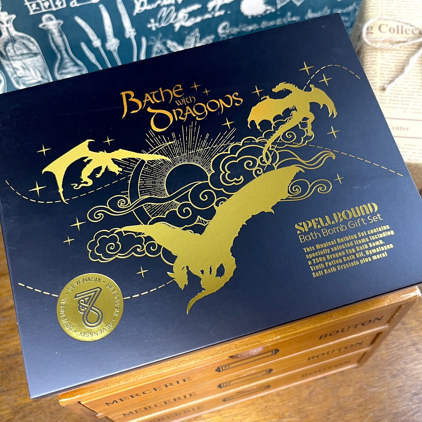 Bathe with Dragons fantasy bath gift box featuring golden lettering, dragon motifs, and contents including dragon egg bath bomb, crystals, mini bath bombs, and potion vial