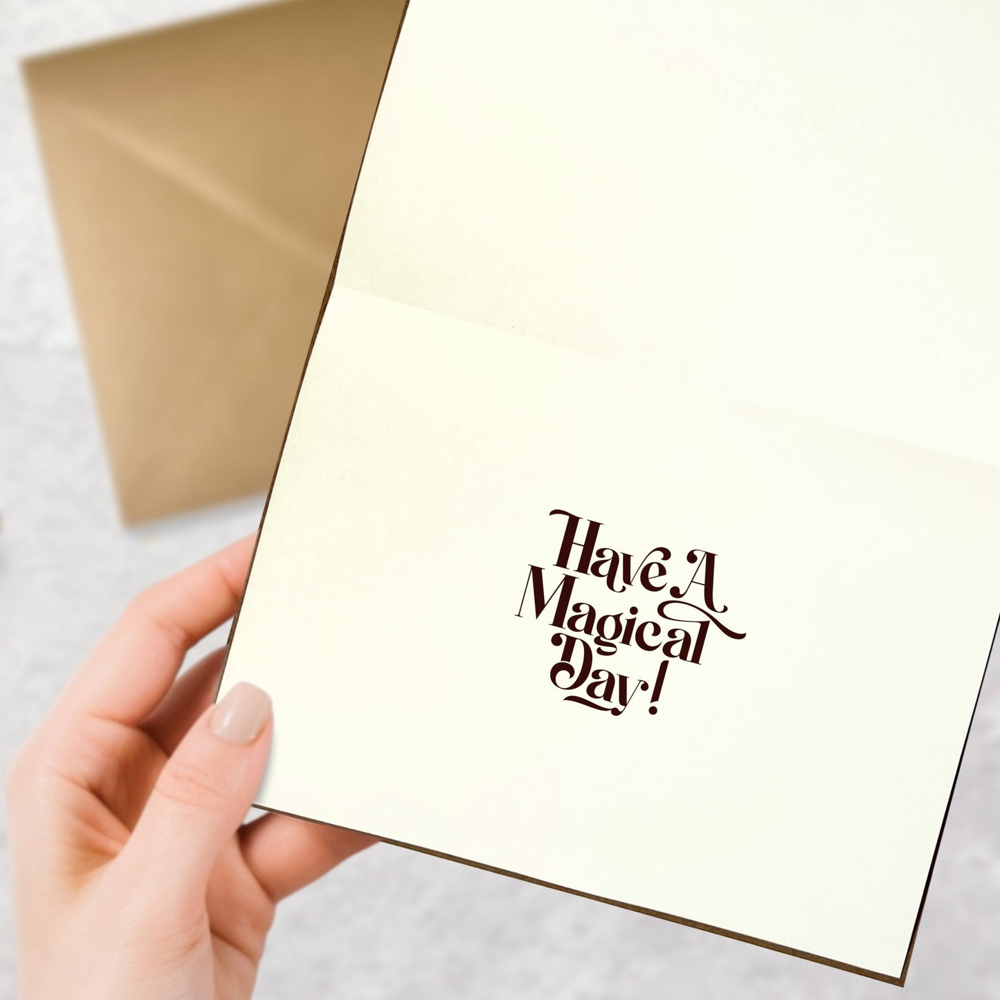 Woman’s hand holding a magical greeting card open with the message ‘Have a Magical Day,’ kraft envelope in the background