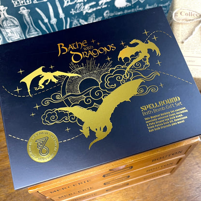 Bathe with Dragons fantasy bath gift box featuring golden lettering, dragon motifs, and contents including dragon egg bath bomb, crystals, mini bath bombs, and potion vial